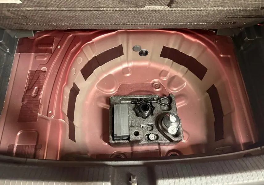 Vue plongeante sur le coffre ouvert d'une Volkswagen Polo Rouge Roi, montrant la zone de rangement sous le plancher sans roue de secours.