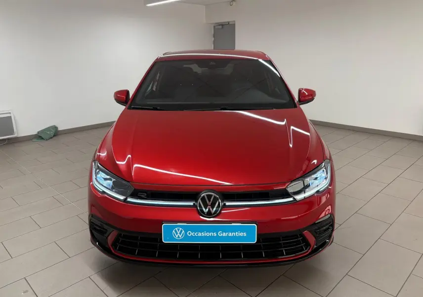 Vue frontale d'une Volkswagen Polo 1.0 TSI R-Line rouge métallisé, avec calandre noire et phares LED allumés.