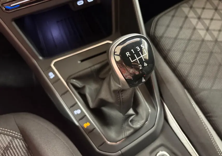 Gros plan sur le levier de vitesses manuel de la Volkswagen Polo 1.0 TSI R-Line, entouré de sièges tissu gris à surpiqûres blanches.