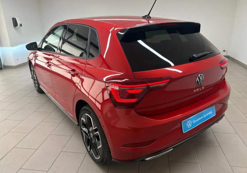 Vue 3/4 arrière droite d'une Volkswagen Polo 2025 Rouge Roi métallisée avec jantes R-Line et vitres teintées.