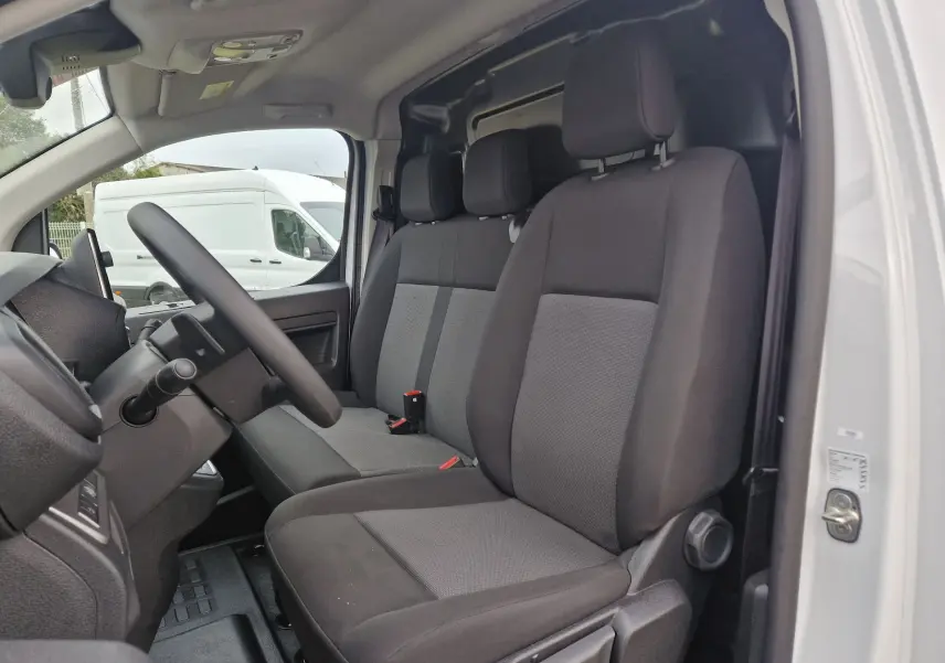 Vue intérieure côté conducteur du FIAT Scudo Fourgon blanc 2024, montrant les sièges tissu gris et noir, avec tableau de bord partiel.