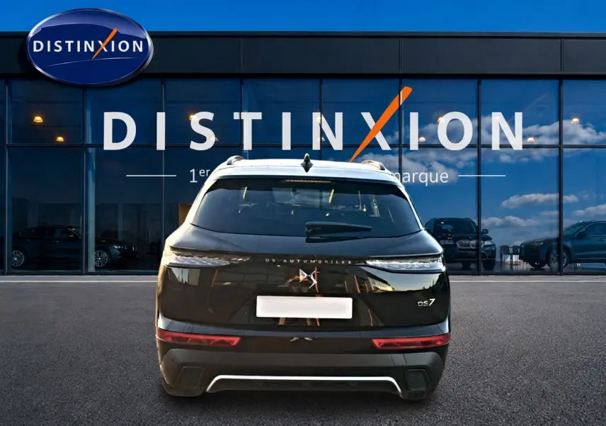 Vue arrière d’un DS7 noir 2026 garé devant une vitrine avec logo Distinxion visible en reflet.