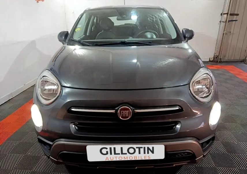 Vue frontale d'une FIAT 500X gris foncé avec phares allumés dans un garage intérieur.