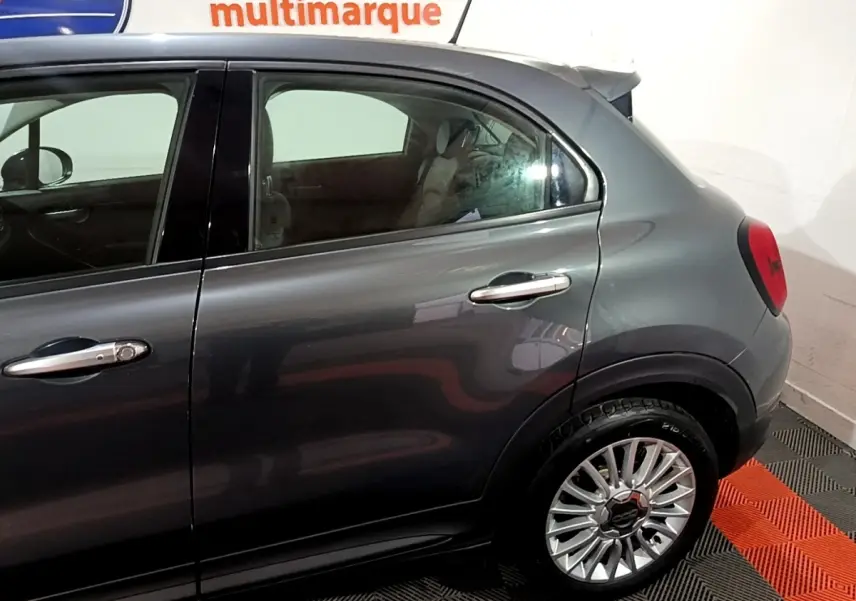 Vue latérale côté droit sur la partie arrière d'une FIAT 500X gris foncé avec jante alliage et poignées chromées.