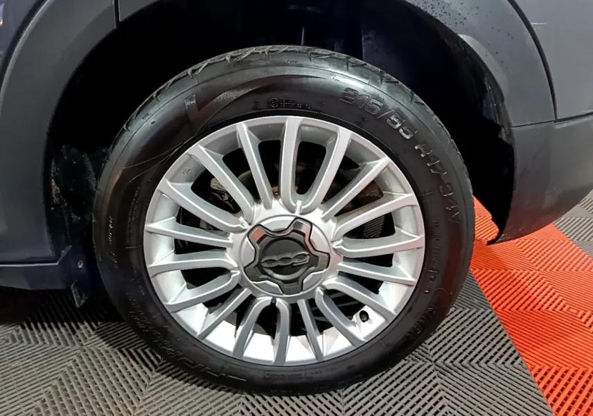 Gros plan sur la roue avant droite d’un FIAT 500X gris foncé, mettant en valeur la jante alliage argentée au design étoilé.