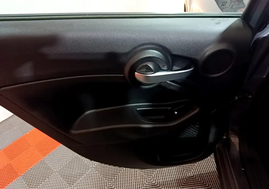 Vue intérieure du panneau de porte côté droit de la FIAT 500X gris foncé, mettant en valeur la poignée argentée et la commande de vitre.