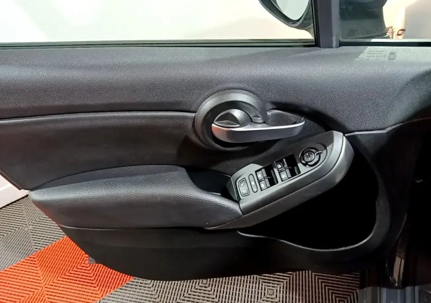 Gros plan sur la porte côté conducteur noire de la FIAT 500X avec commandes électriques des vitres et poignée argentée.