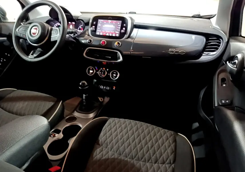 Vue intérieure avant du tableau de bord gris foncé et des sièges tissu matelassé de la Fiat 500X 1.6 Multijet 2019.