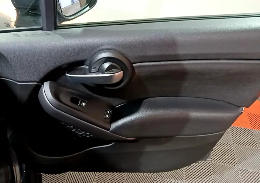 Vue rapprochée de la porte côté conducteur d'une FIAT 500X gris foncé, avec poignée argentée et commandes de vitres.
