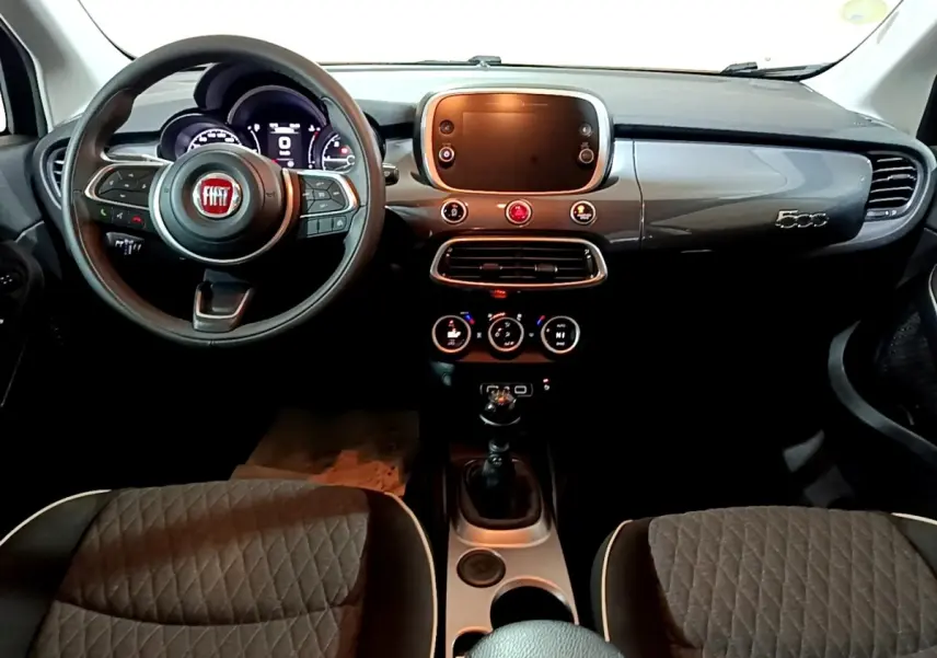 Vue intérieure avant du tableau de bord gris brillant et volant noir de la Fiat 500X avec écran tactile et sièges tissu gris.