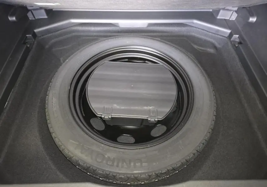 Roue de secours galette noire dans le coffre d’un Peugeot 3008 gris, vue plongeante centrée.