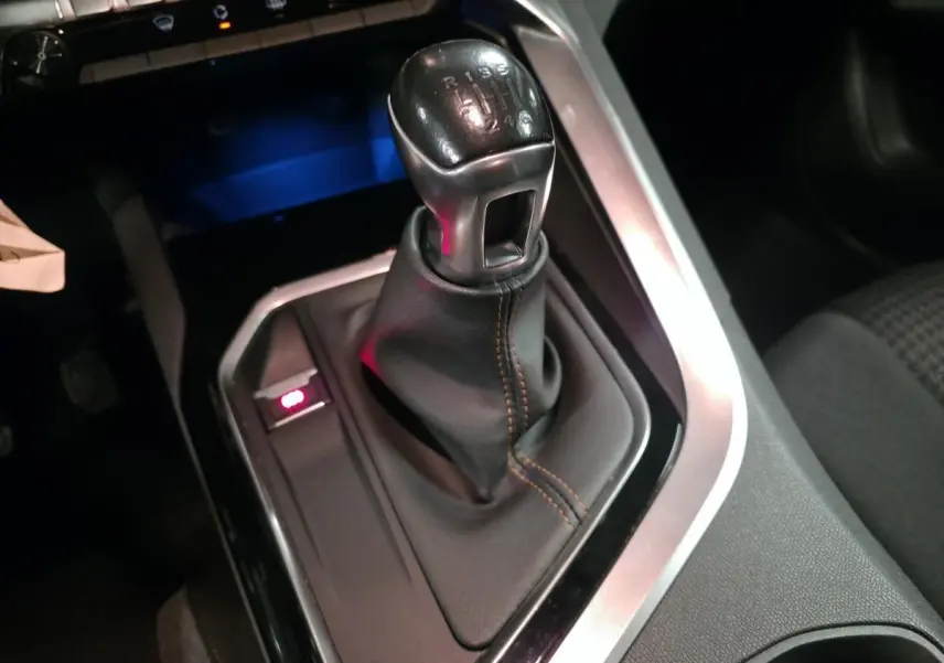 Gros plan sur le levier de vitesses manuel noir avec surpiqûres marron dans le Peugeot 3008 gris.