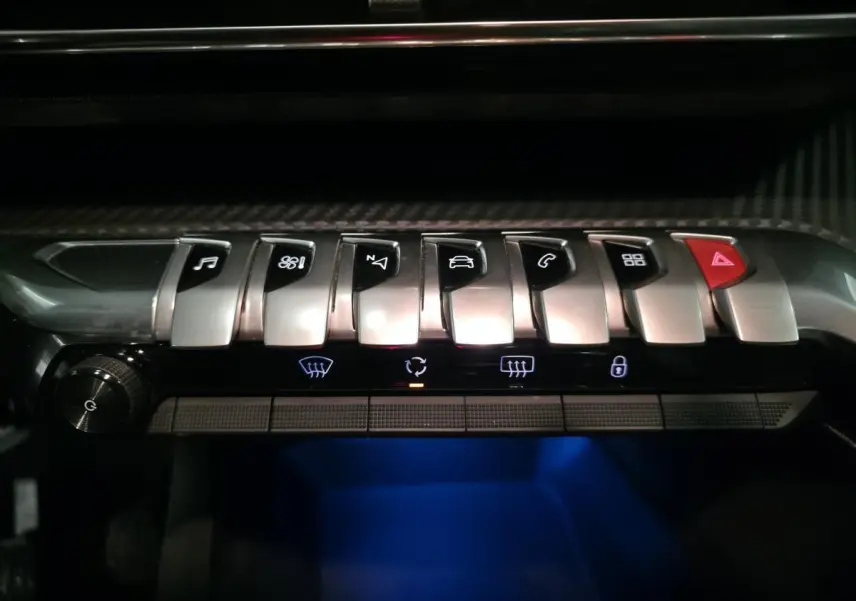 Gros plan sur les commandes chromées et boutons tactiles du tableau de bord du Peugeot 3008 gris, éclairage bleu dessous.