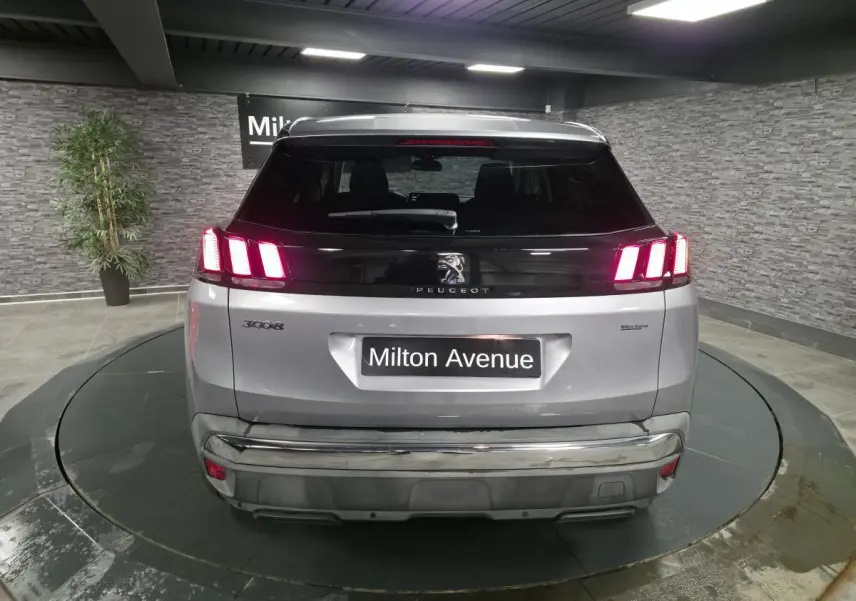 Vue arrière d'un Peugeot 3008 gris métallisé avec feux arrière allumés et bandeau noir brillant sur le hayon.