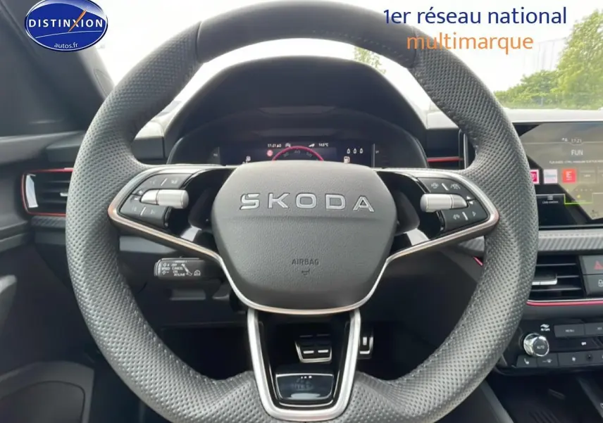 Vue rapprochée du volant cuir perforé SKODA avec commandes multifonctions et tableau de bord numérique en arrière-plan.