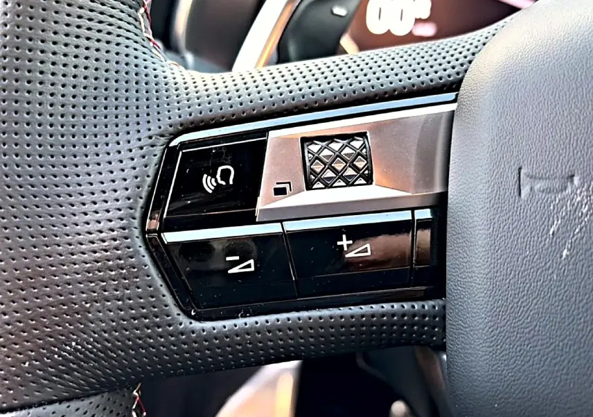 Gros plan sur les commandes gauche du volant cuir perforé du DS7 noir, avec boutons de volume et molette tactile.