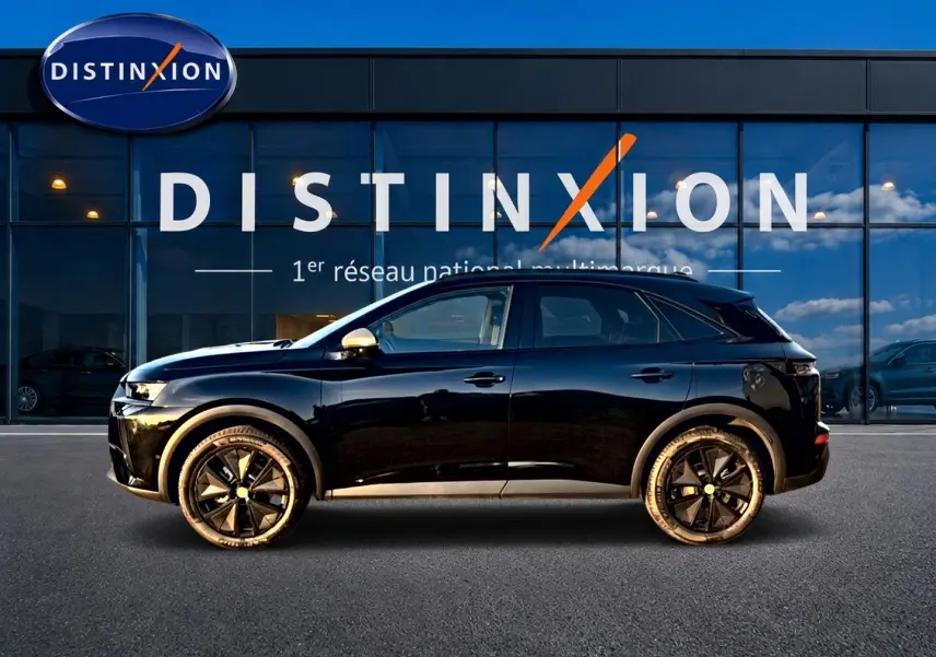 Vue latérale droite d’un DS7 noir brillant avec jantes noires, garé devant une vitrine Distinxion.