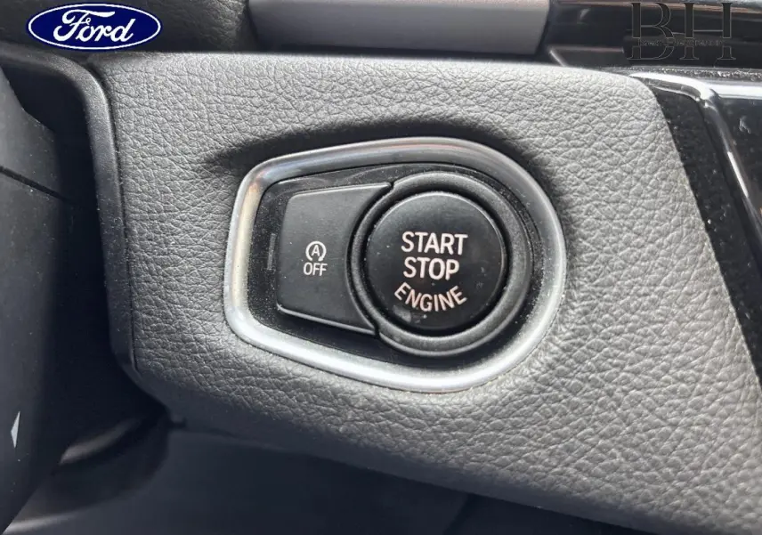 Bouton start-stop moteur en gros plan sur tableau de bord noir texturé, entouré d’un cadre argenté.