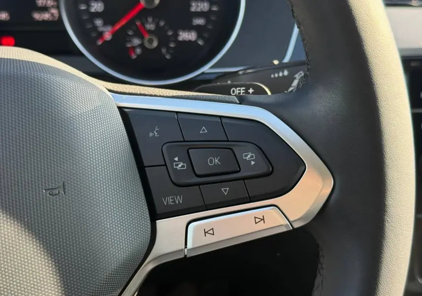 Gros plan sur les commandes multifonctions à droite du volant cuir de la Volkswagen Passat SW noire, avec tableau de bord partiellement visible.