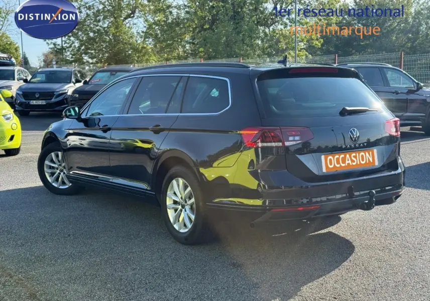 Volkswagen Passat SW noir intense nacré vue 3/4 arrière droit avec barres de toit et attelage visible.