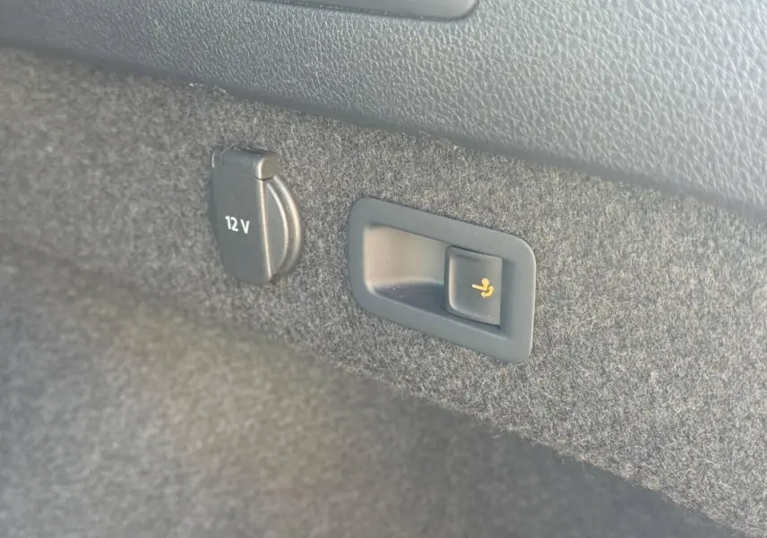 Détail intérieur du coffre de la Volkswagen Passat SW noir nacré montrant prise 12V et bouton rabattage siège arrière.