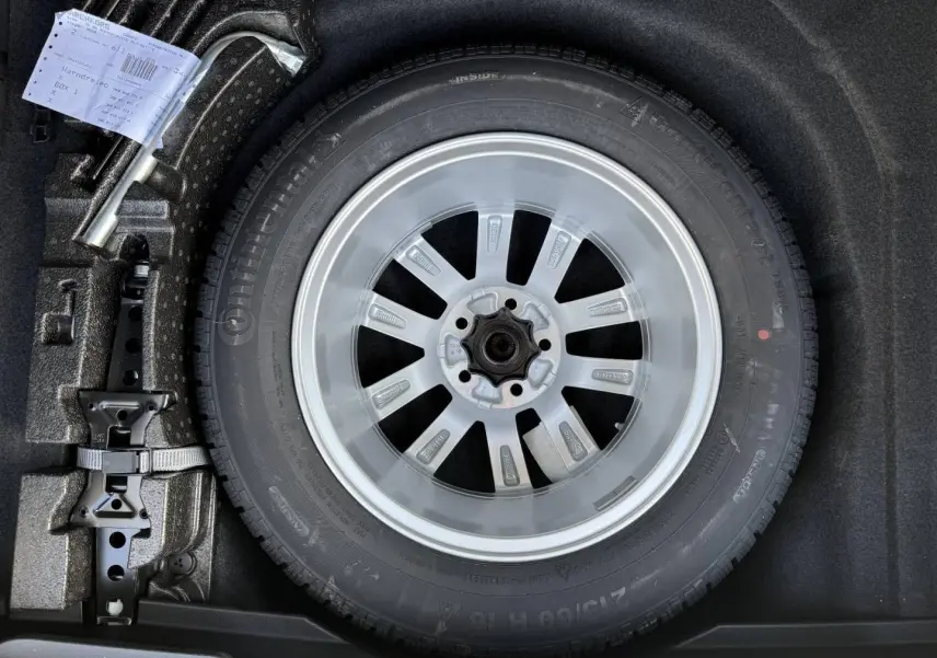 Gros plan sur la roue de secours avec jante acier et cric dans le coffre d’une Volkswagen Passat SW noire.