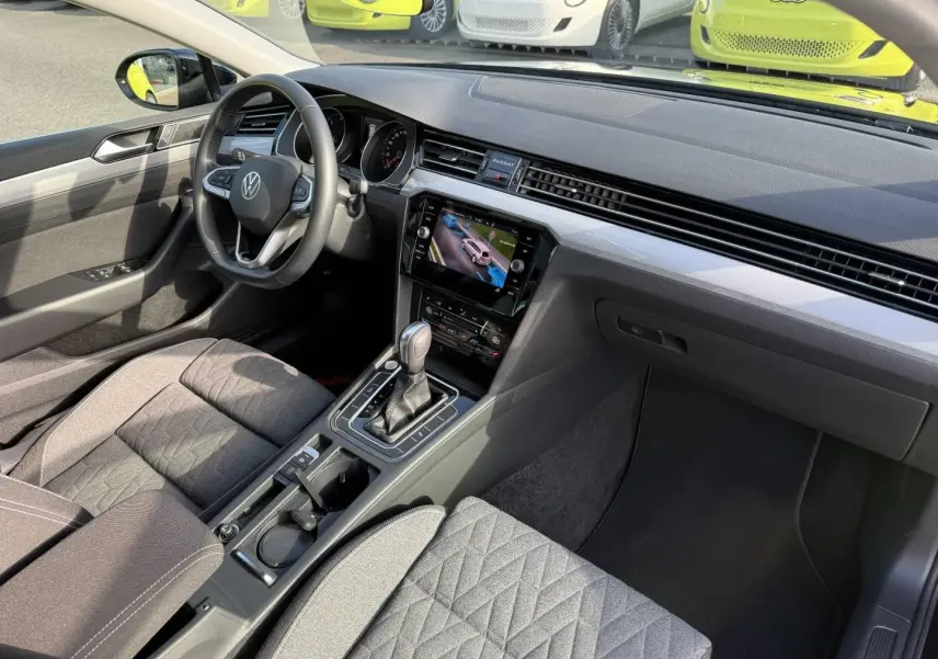 Vue intérieure côté conducteur de la Volkswagen Passat SW 2.0 TDI Business avec tableau de bord moderne et sièges tissu noir.