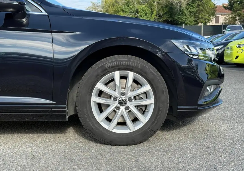 Gros plan sur la roue avant droite et partie avant d'une Volkswagen Passat SW noire nacrée, avec jante alu et phare LED visible.