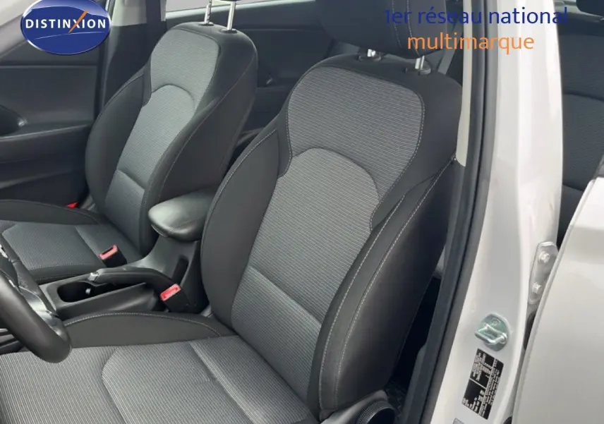 Vue intérieure côté conducteur d'une Hyundai i30 blanc nacré 2023, sièges tissu gris et noir avec accoudoir central.