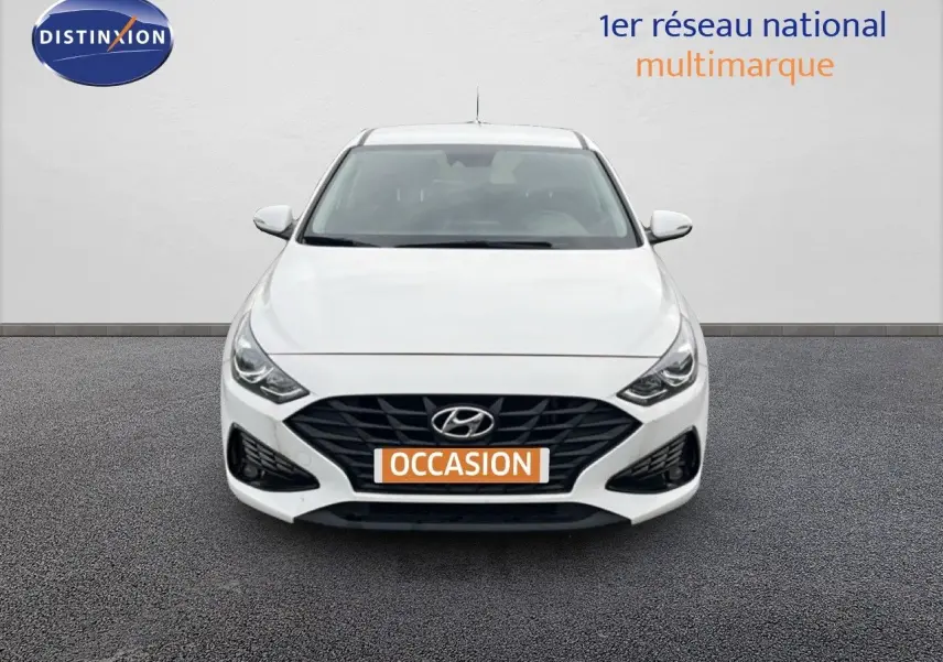 Vue de face d'une Hyundai i30 blanche nacrée avec calandre noire et plaque "OCCASION" orange.