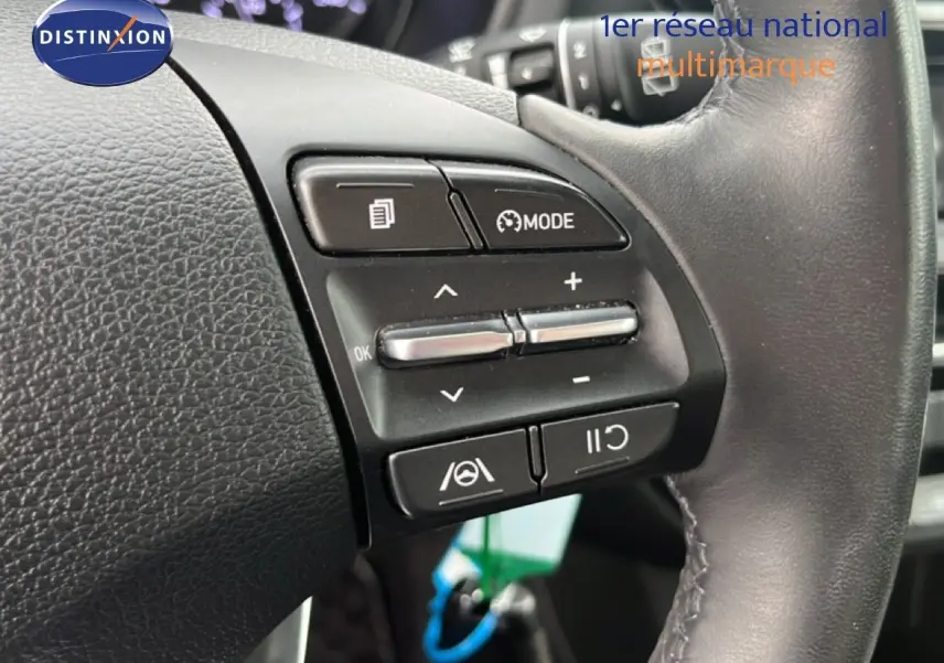 Gros plan sur les commandes au volant d'une Hyundai i30 2023, finition Confort, avec cuir noir et boutons multifonctions.