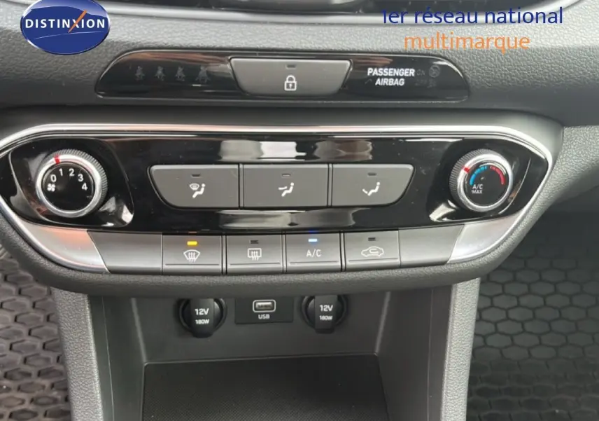 Vue rapprochée de la console centrale de la Hyundai i30 blanche nacrée, montrant les commandes de climatisation et ports USB et 12V.