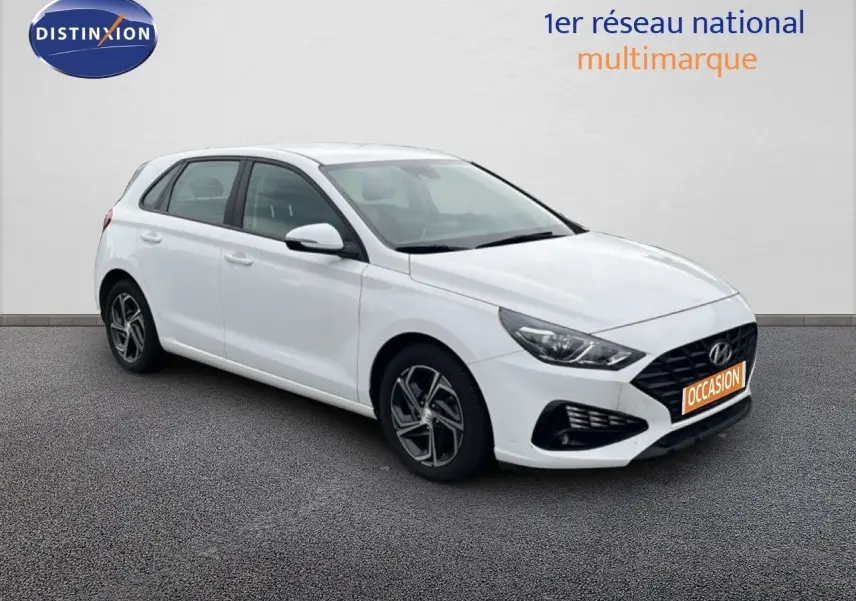 Vue 3/4 avant droit d'une Hyundai i30 blanche nacrée 5 portes, avec jantes alliage et calandre noire distinctive.