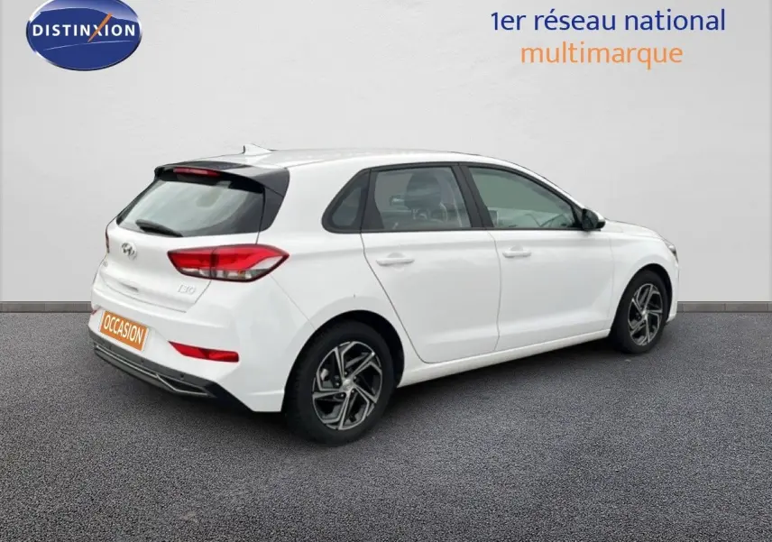Vue 3/4 arrière droite d'une Hyundai i30 blanc nacré 2023, compacte 5 portes avec jantes alliage bicolores.