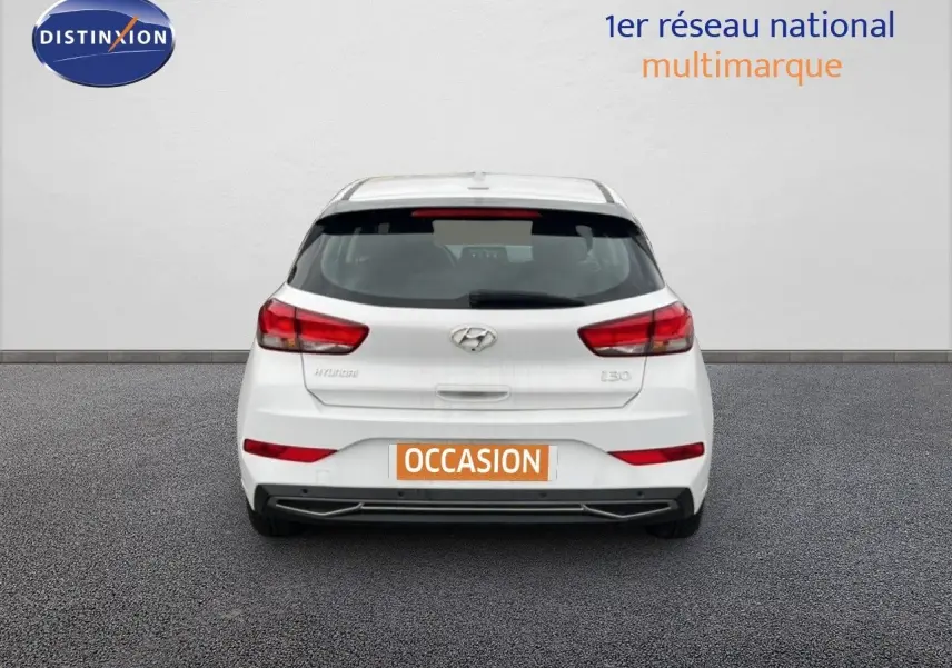 Vue arrière d'une Hyundai i30 blanche nacrée 2023, compacte avec feux arrière rouges et plaque "OCCASION" visible.