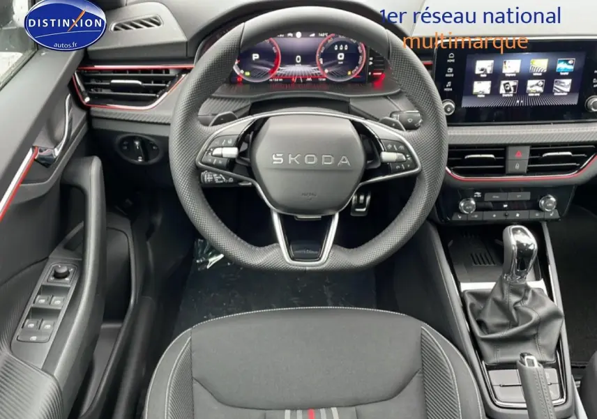 Vue intérieure centrée sur le volant SKODA et tableau de bord numérique avec console centrale et levier de vitesse.