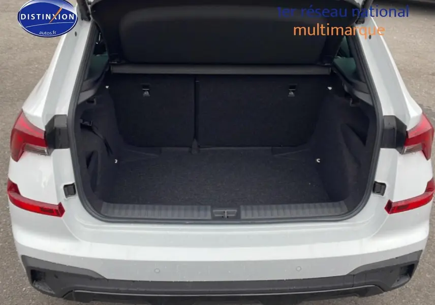 Coffre ouvert vu de l'arrière d'un Skoda Kamiq blanc nacré avec hayon électrique et feux arrière LED visibles.