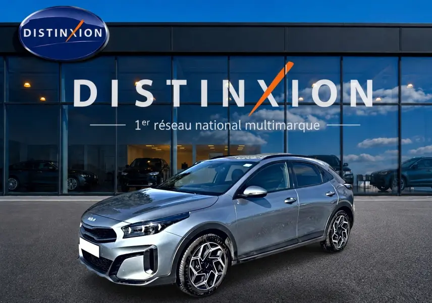 KIA Xceed gris en 3/4 avant droit, avec jantes alu distinctives, stationné devant une vitrine Distinxion.