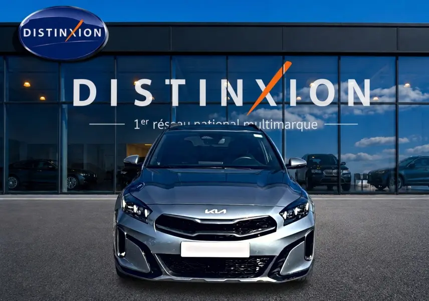 Vue frontale d'une KIA Xceed gris métallisé avec calandre chromée et feux LED, devant une vitrine Distinxion.