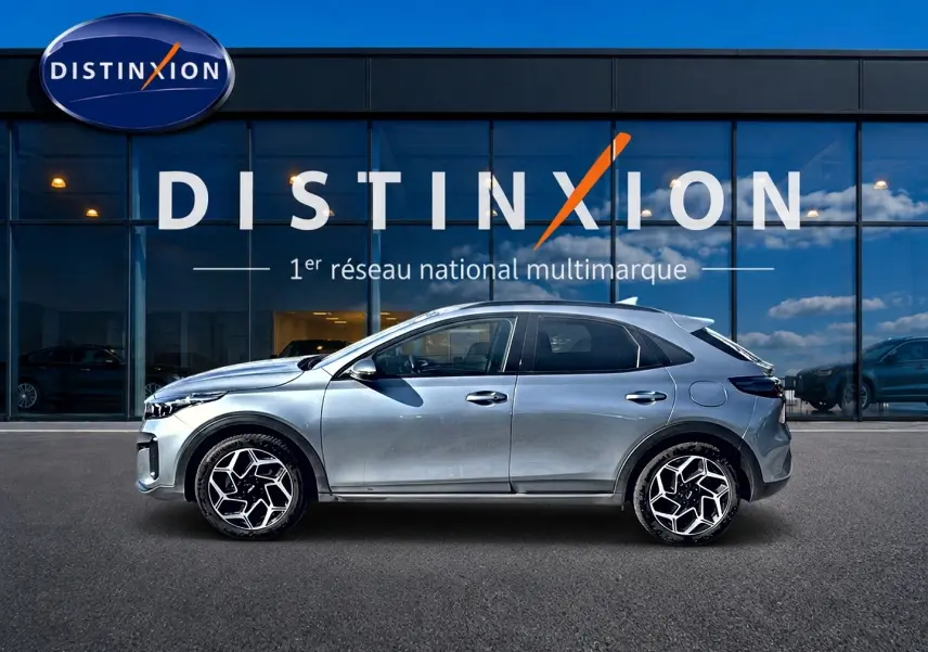 Vue latérale droite d'un KIA Xceed gris 2024 avec jantes alliage au design géométrique devant un showroom Distinxion.