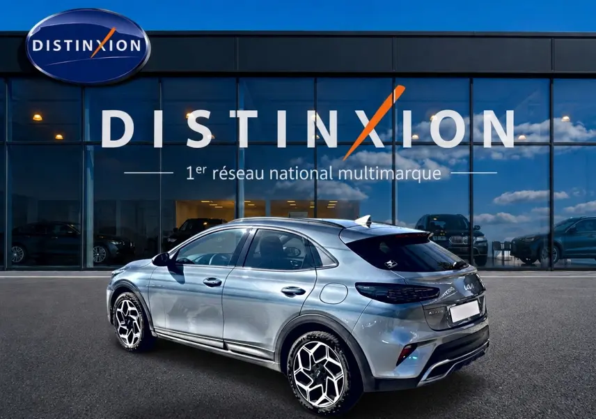 Vue 3/4 arrière droite d'un KIA Xceed gris 2024 avec jantes alu et becquet arrière, devant une vitrine Distinxion.