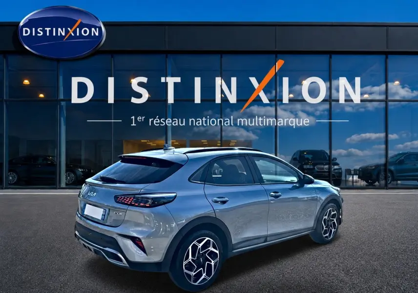 Vue 3/4 arrière droite d'un KIA Xceed gris 2024 avec jantes alu et becquet arrière, devant une vitrine Distinxion.