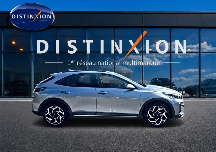 KIA Xceed gris en profil droit, avec jantes alu distinctives et calandre chromée visible devant un showroom Distinxion.