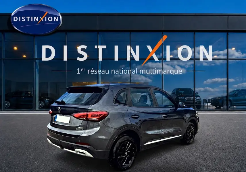 MG ZS 1.5 hybrid 197 gris Camden en 3/4 arrière droit, avec jantes noires et becquet arrière visible devant showroom Distinxion.