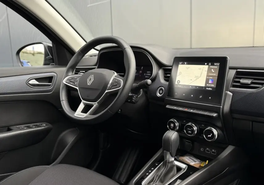 Vue intérieure côté conducteur du Renault Arkana bleu Zanzibar, avec volant multifonction, écran tactile GPS et levier de boîte auto.