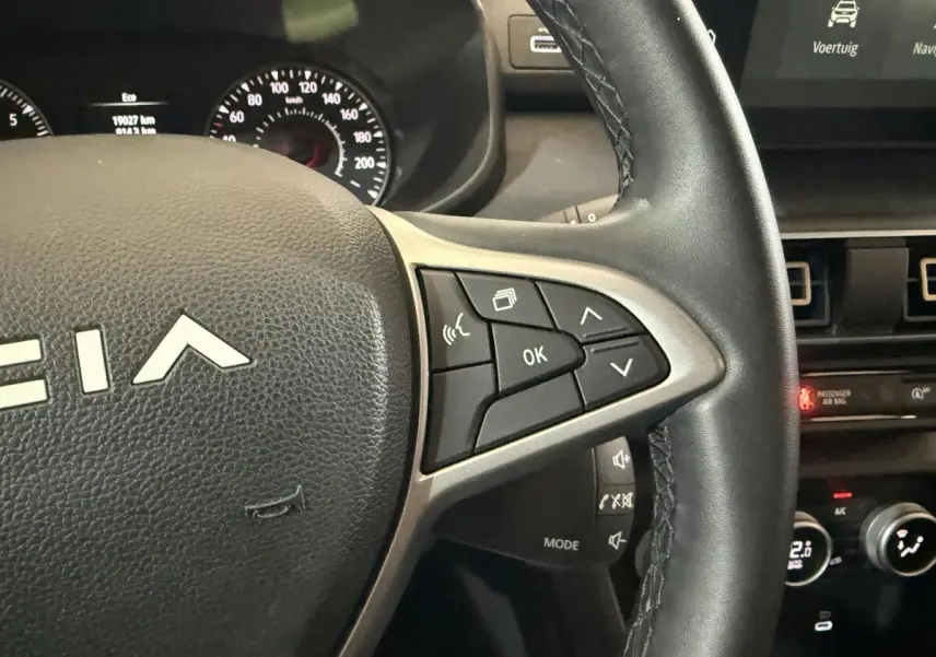 Gros plan sur le volant en cuir synthétique de la Dacia Sandero 2024, avec commandes multifonctions visibles côté droit.