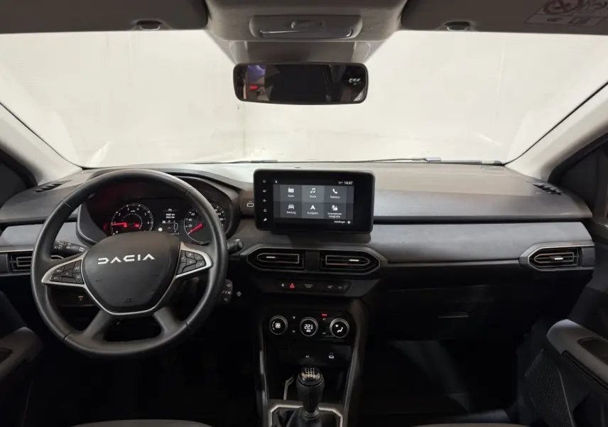 Vue frontale de l'intérieur du Dacia Sandero 2024 avec volant cuir multifonctions et écran tactile central.