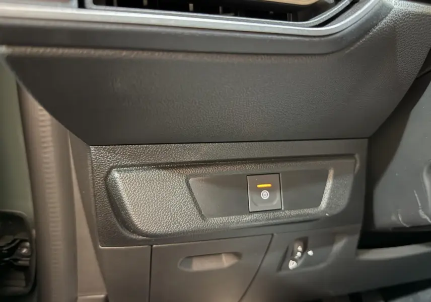 Gros plan sur le bouton de frein à main électrique orange dans l'habitacle noir de la Dacia Sandero Extreme+ 2024.