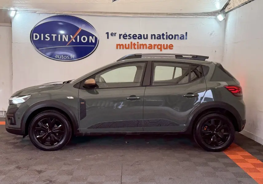 Vue de profil côté gauche d'une Dacia Sandero Extreme+ TCe 110 2024 vert foncé avec jantes noires et barres de toit.