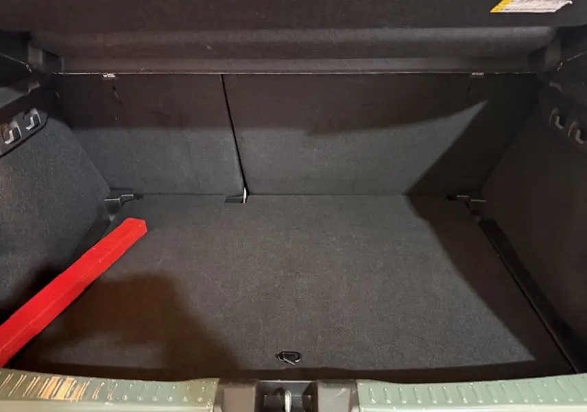 Coffre ouvert de la Dacia Sandero Extreme+ TCe 110 2024 vert, avec tapis noir et triangle de signalisation rouge.